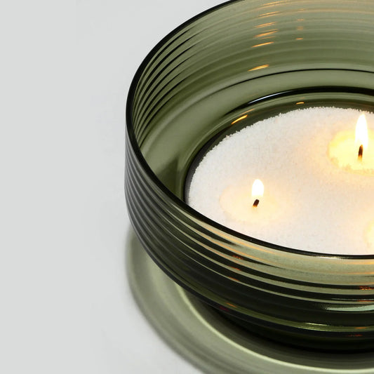 Green ribbed glass candle holder with two lit candles in white sand