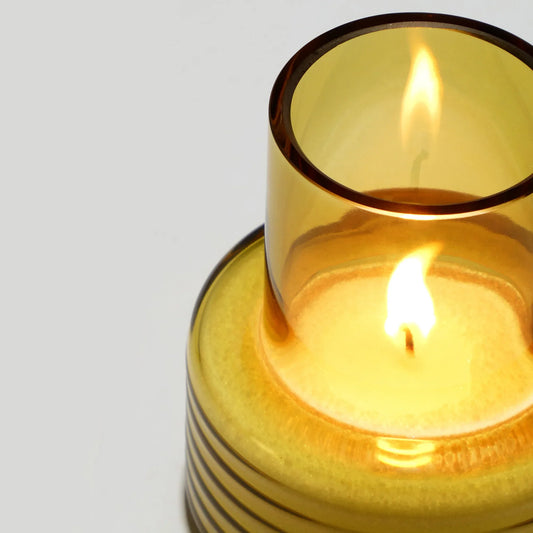 Close-up of a mustard yellow blown glass candle holder with lit candle, modern decor.