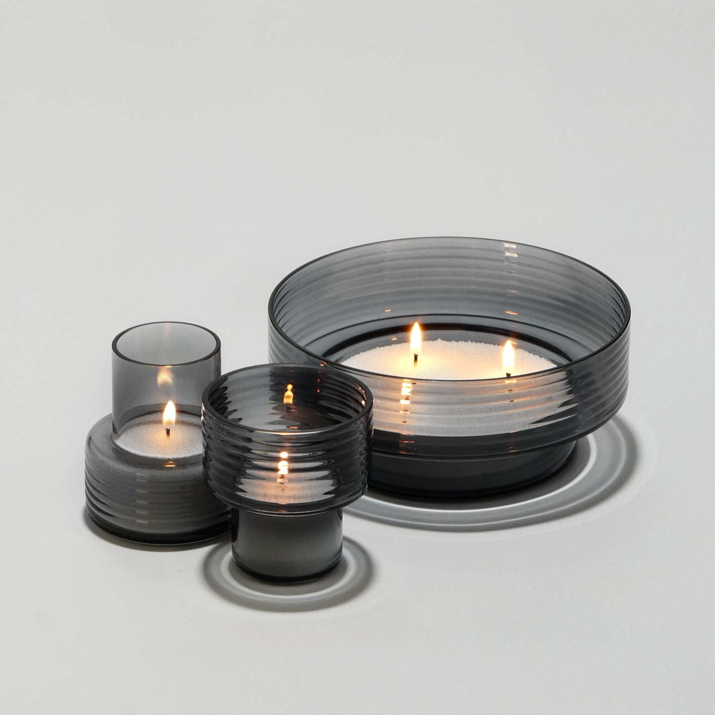 Set of three ribbed smoked glass candle holders with lit candles on white background