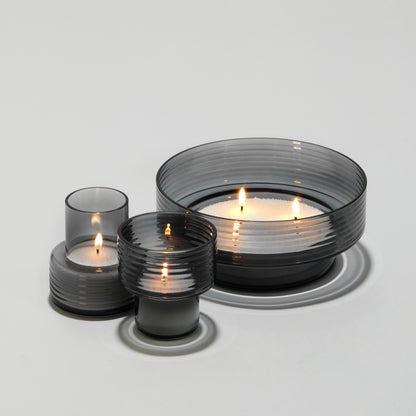 Set of three ribbed smoked glass candle holders with lit candles on white background